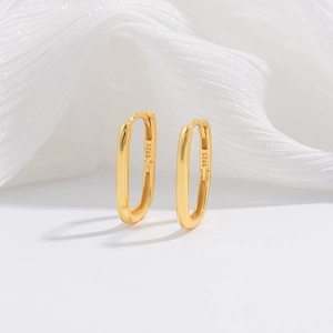 Close-up of S925 hallmark on gold bamboo-style oval hoop earrings on white silk background