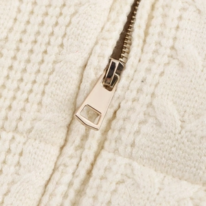 Close-up of light gold metal zipper on white chunky knit stand collar vest