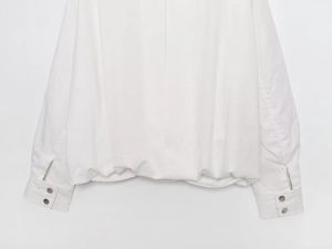 Detail of double-button cuffs and loose hem on white long-sleeved bomber jacket