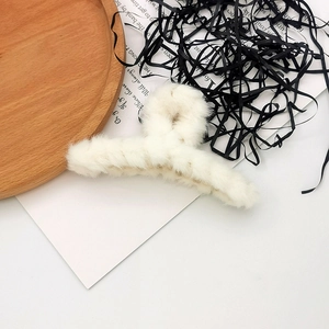 Detail shot of a plush white faux fur claw clip on a rustic wooden tray with soft textures