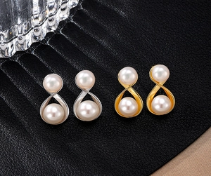 Macro shot of S925 silver infinity pearl studs in gold and silver on black leather