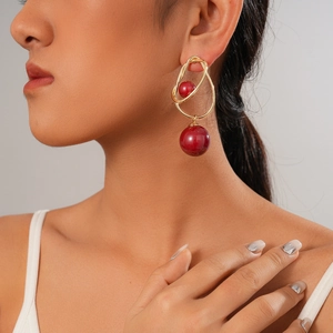 Vintage style gold metal earrings with red beads and irregular ring design worn by model