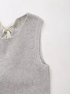 Détail du gilet en maille grise avec un nœud en ruban blanc sur le col arrière