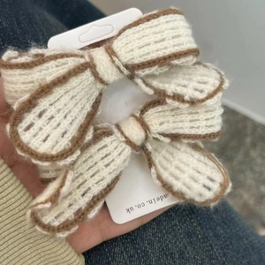 Pair of handmade knit bow hair clips in cream yarn with brown edges on display card