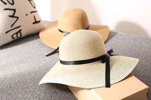Detail showing two wide-brim woven straw sun hats with elegant black ribbon bow tie