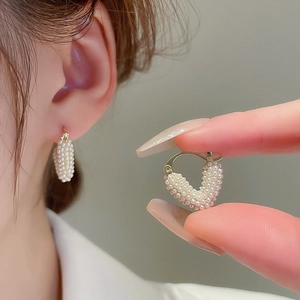 Elegant heart-shaped pearl earrings in gold finish worn by model for scale