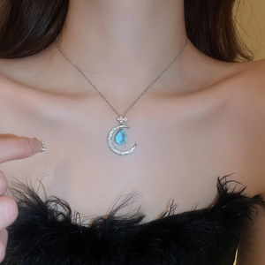 Detailed close-up of water drop blue gemstone and crescent moon pendant on female neck