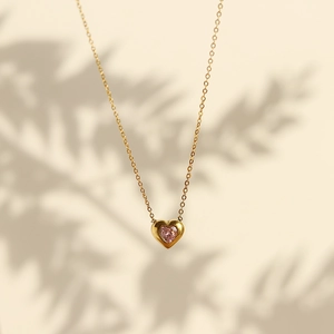 Close-up of golden heart pendant necklace with pink gemstone and soft leaf shadows