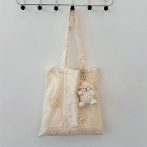 Close-up of cream canvas tote bag featuring floral lace embroidery and a plush sheep charm
