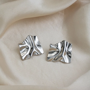 Irregular silver pleated earrings with geometric texture on elegant beige silk fabric