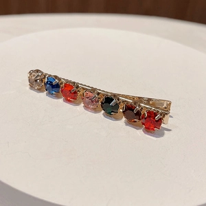 Detail shot of a golden alloy hair clip featuring seven colorful sparkling rhinestones