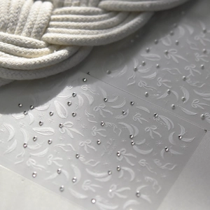 Primer plano de pegatinas 3D para uñas con lazos blancos, cintas y pequeñas perlas