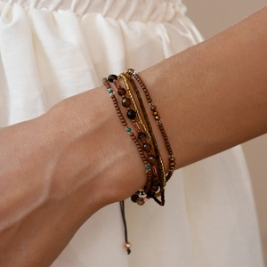 Detailopname van een gelaagde kralenarmband met bruine en gouden glazen agaten