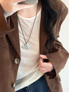 Macro view of vintage silver ginkgo leaf pendant on brown cord with detailed textures
