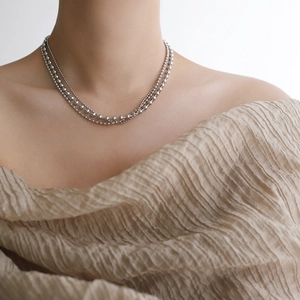 Detail of layered silver beaded necklace with polished finish on beige fabric background