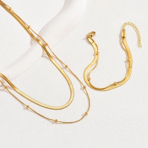 Elegantes Set aus goldener Schlangenkette und passendem Armband auf weißem Hintergrund