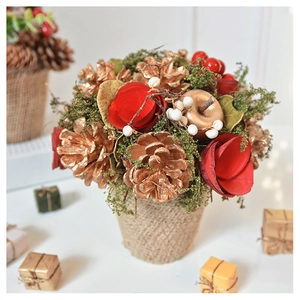 Detail view of festive table decor with golden pinecones, red flowers, and burlap base