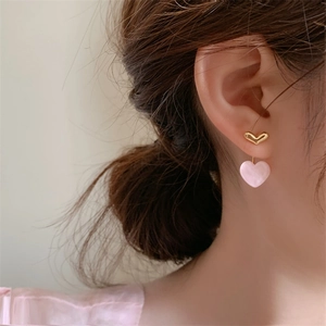 Close-up of pink heart stud earrings with gold finish on a model's ear
