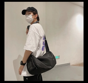 Black nylon gym bag featuring side zipper pocket and adjustable shoulder strap worn by model