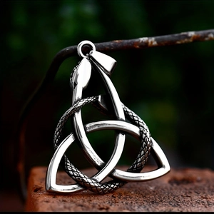 Detail of silver Celtic Triquetra knot and snake pendant on a dark stone background