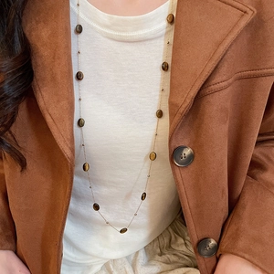 Close-up of tiger eye beaded necklace with gold chain worn over a brown jacket