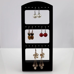 Three-tier black display stand with assorted pearl, pineapple, and floral tassel earrings