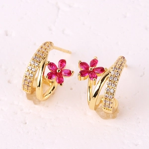 Macro detail of a gold flower stud earring with red zircon petals and clear crystals