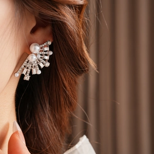 Macro shot of silver fan-shaped earrings with pearls and crystals on a model