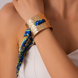 Dettaglio di bracciale rigido dorato con foulard di seta blu intrecciato nel metallo