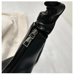 Close-up of smooth silver metal zipper and black pleated cloud-style handle on handbag