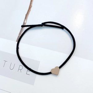 Detailed view of black elastic hair tie with a brown resin heart bead on textured background