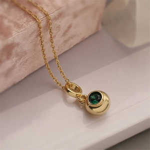 Close-up of gold chain necklace with round pendant featuring a sparkling green gemstone