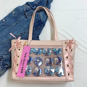Pink ita bag with clear window showing anime badges and ribbon lace-up detail on the side