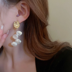 Elegant gold textured disk with four long hanging baroque pearls on model's ear