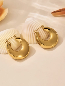 Détail de boucles d'oreilles créoles dorées épaisses au fini poli sur fond de coquillage