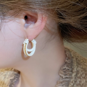 Detail shot of white and gold twisted rope hoop earrings worn on ear with knit outfit