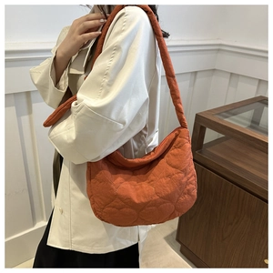 Detail of an orange quilted tote bag with heart patterns worn with a beige trench coat