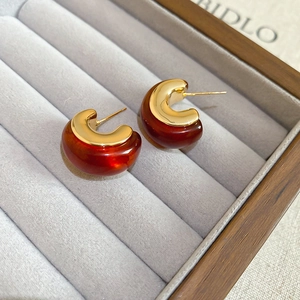 Detail of 18k gold plated and amber resin C-shape earrings on jewelry display tray