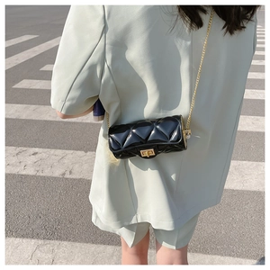 Chic black quilted cylinder bag with gold chain strap shown crossbody on a model outdoors