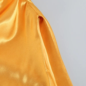 Gros plan sur le tissu en satin doré montrant les coutures et la fente de la robe