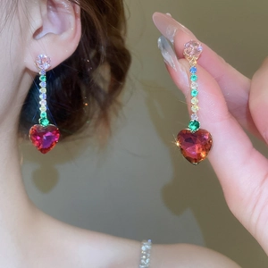 Detailed macro view of gold tassel earrings with colorful zircons and a red heart gemstone