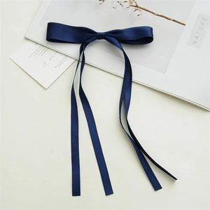 Close-up of dark blue satin bow hair clip with elegant long flowing ribbon tassels