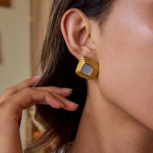 Gros plan de boucles d'oreilles dorées carrées de luxe avec résine grise et blanche