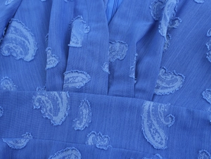 Gros plan sur le tissu bleu de la robe avec jacquard cachemire et plis à la taille