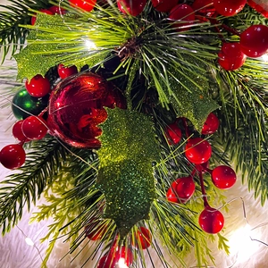 Detail of Christmas teardrop swag with red berries, pine needles and warm LED string lights