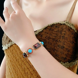 Detail view of a vintage gold bracelet with ruby-red stones and turquoise gems on a wrist