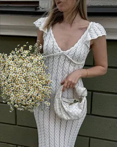 Détail d'une robe en maille crochetée blanche avec col en V, volants et sac à main tissé