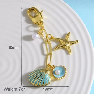 Dettaglio del portachiavi dorato a tema marino con conchiglia blu e misure di 82mm x 19mm