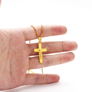 Detailed view of a gold-plated cross pendant with Jesus relief held in hand for scale
