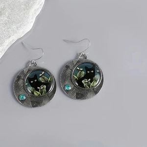 Detail of vintage silver earrings featuring a black cat pattern and a blue gemstone